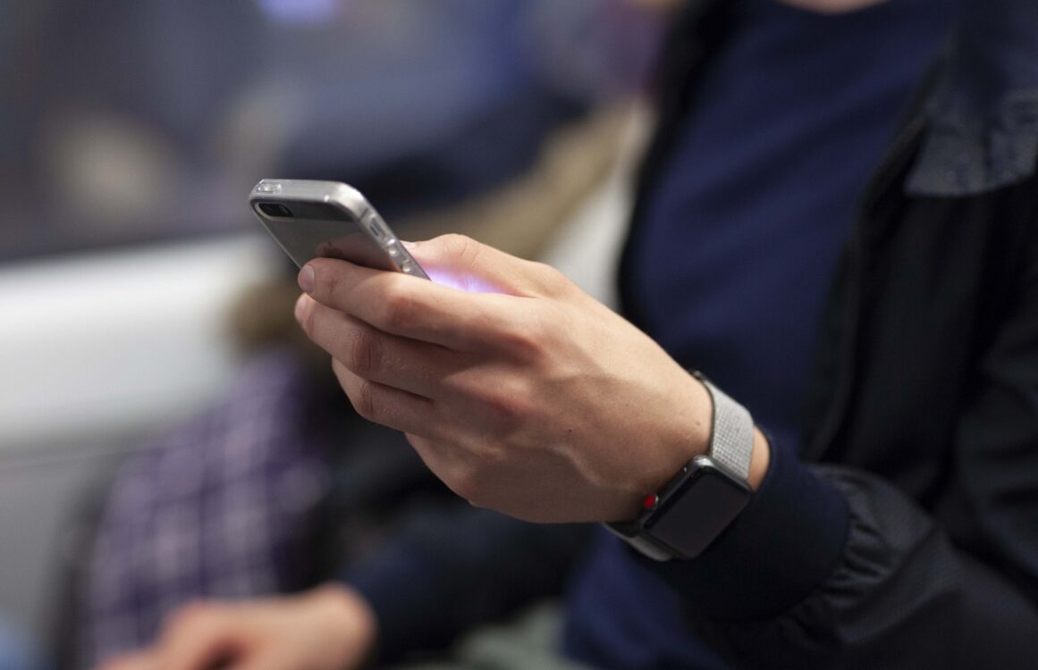 Mann mit Smartwatch am Handgelenk und Smartphone in der Hand Detailansicht