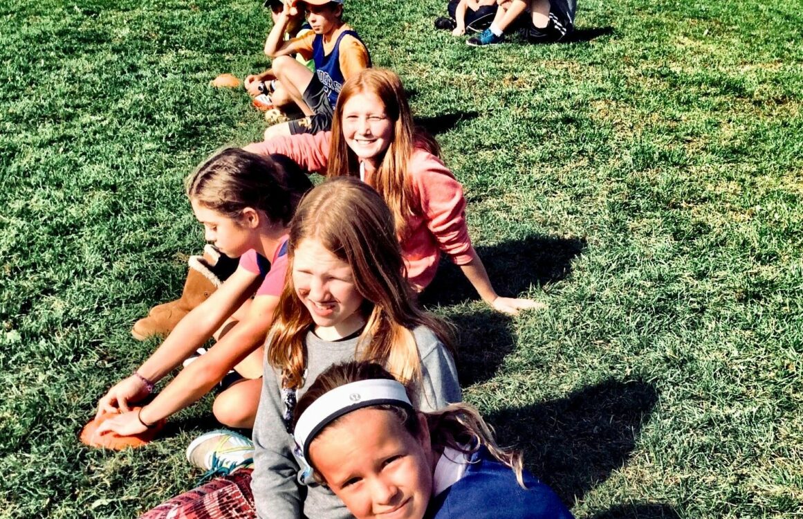Kinder sitzen nebeneinander auf einer Wiese