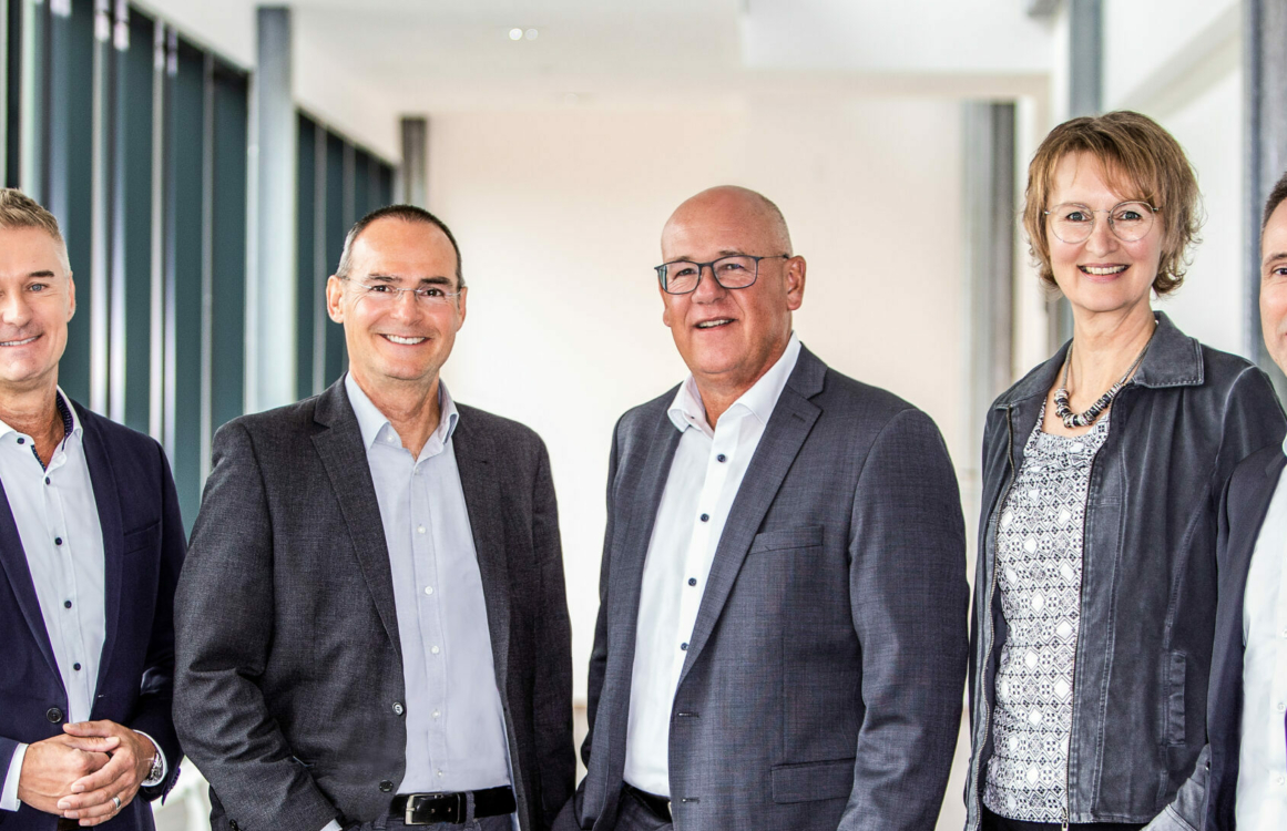 Kollegin und Kollegen in Anzügen posieren nebeneinander