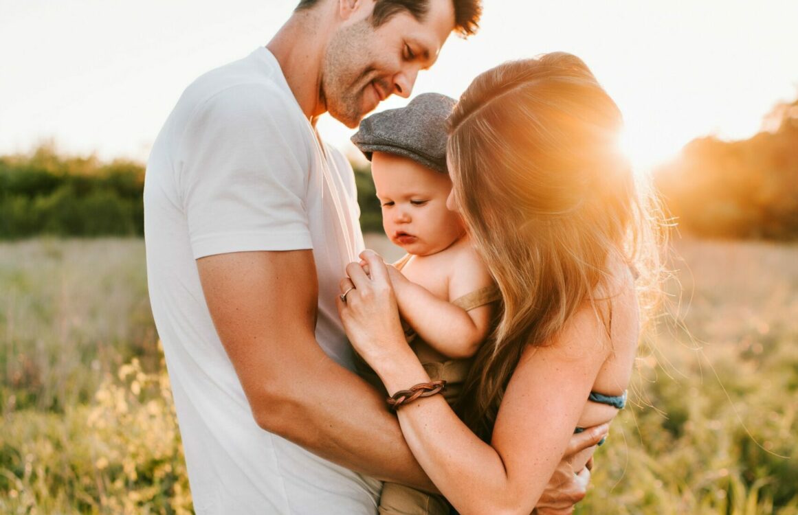Eltern mit Kind im Arm einer einer Wiese