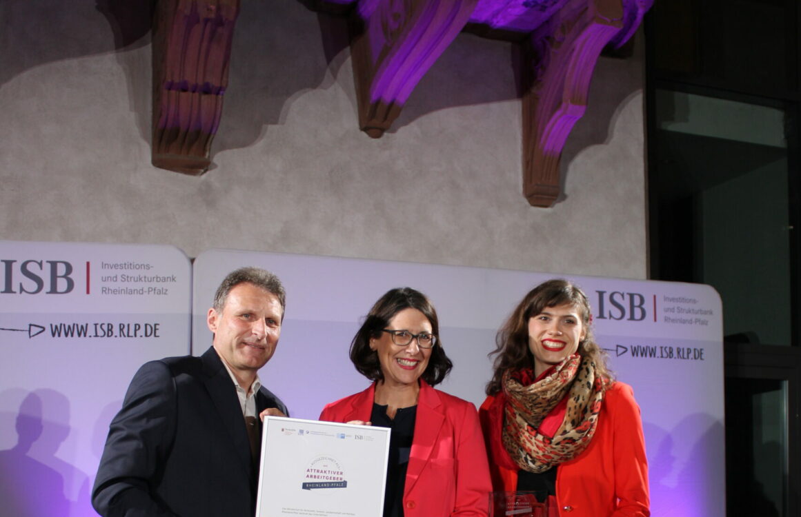 Drei Menschen bei der Übergabe einer Urkunde auf der Bühne